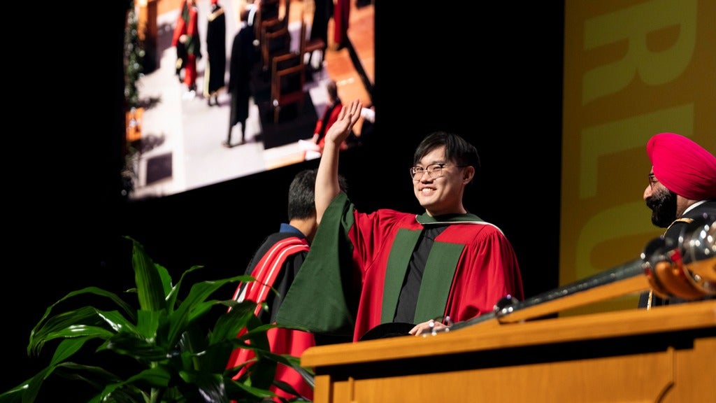 PhD graduate waves to crowd while crossing the stage at convocation