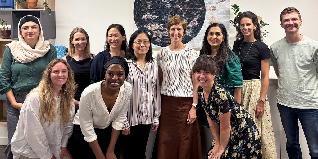 Eleven people pose together in front of a circular frame of art