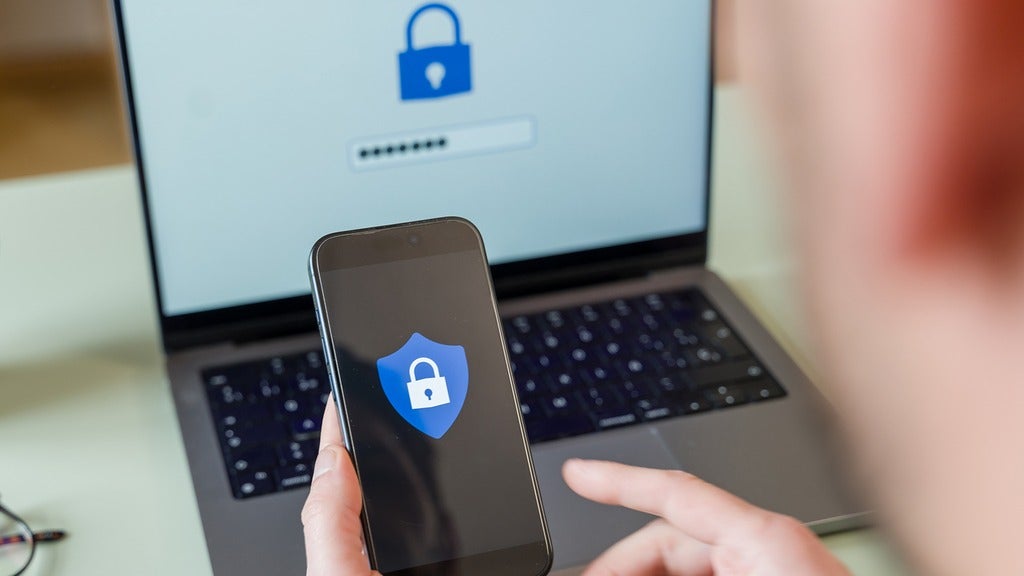 Over the shoulder of someone using a laptop and mobile device both screens have a lock displayed on them