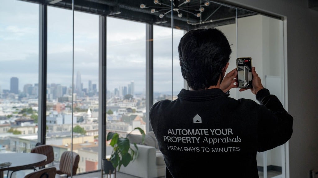 person with back to camera holds up a phone to scan a wall near a window showing a cityscape.