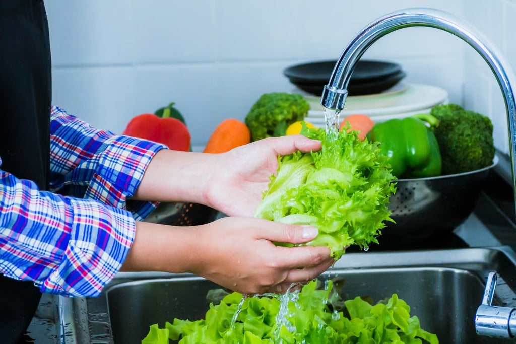 A person washing lettuce under running water (Getty Images/Apichet)