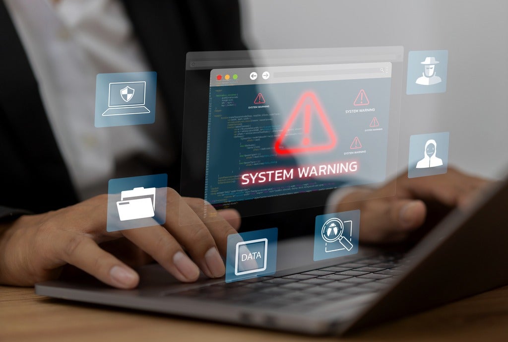 A person types on a keyboard as visual representations of artificial intelligence, cybersecurity threats and system warnings are displayed.