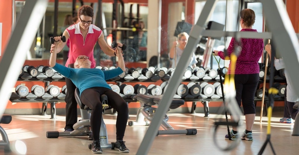 Gym setting with woman on bench press, one assisting, and one to the side