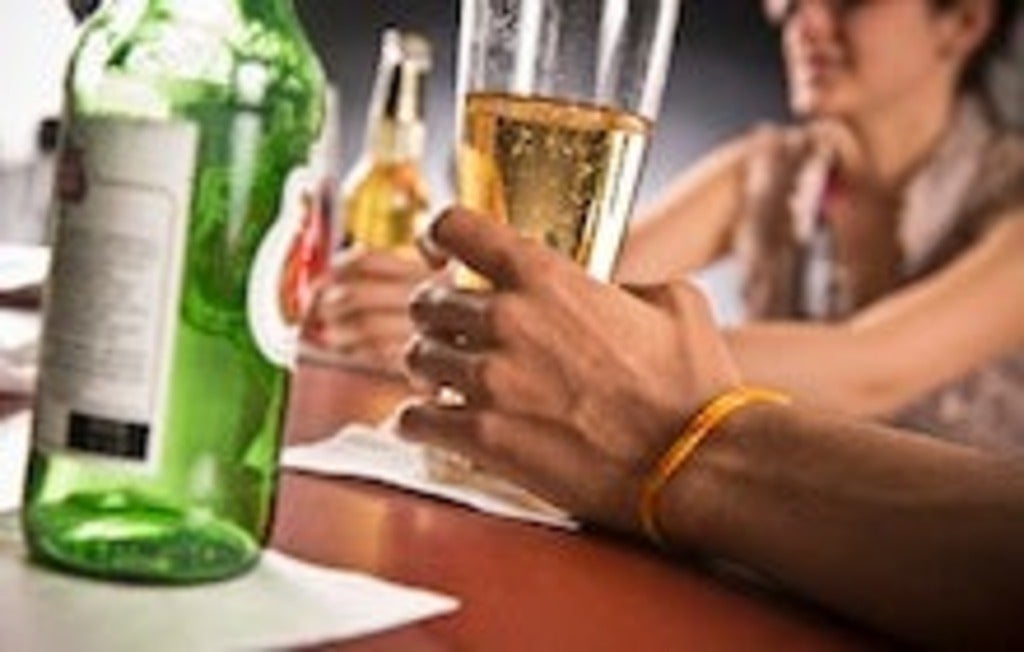 Man's hand holding a glass of beer on a bar.