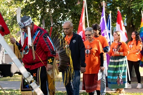 Procession including Myeengun Henry, Vivek Goel and Jean Becker walk into tent at 2023 recommitment ceremony