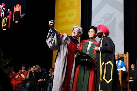 Waterloo graduate stands to take a selfie on stage during convocation 