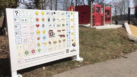 The alternative and augmented communication board near a path and playground structures. Content of the board described in story