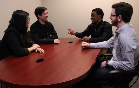 Aaron Cole smiles at colleagues as he speaks to them around a table.