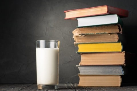 glass of milk stands next to pile of old books