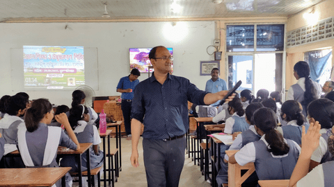 Dr. Rajibul Islam holding a mic addresses students seated at desks in a classroom with a projected presentation at the front.