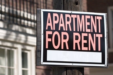 Apartment for rent sign on post in front of a building.