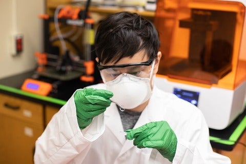 student wearing a mask examining a lens close to his face