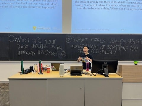 Student in front of a chalkboard smiling with thumbs up