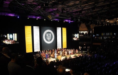 Convocation stage with dignitaries standing and recognizing the crowd