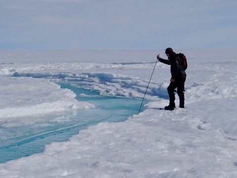 Man inserts measuring stick into a stream on top of ice