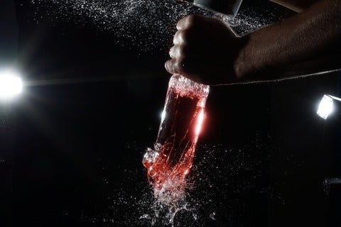 Someone doing the party trick that involves shattering the bottom of a liquid-filled bottle by striking its open top 