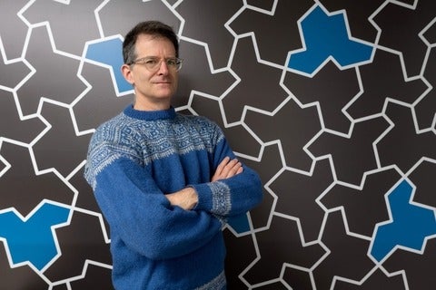 Professor Craig S. Kaplan stands in front of a wall of hat-shaped einstein tiles 