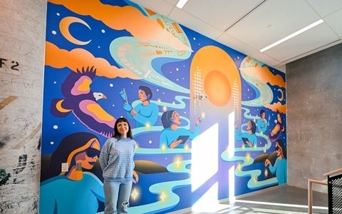 Alanah Jewell standing proudly in front of her Many Hearts, One Mind mural inside the Innovation Arena