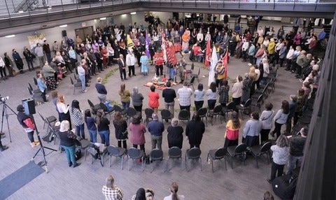 Staff, students and faculty form a circle around the Eagle Staff and elders