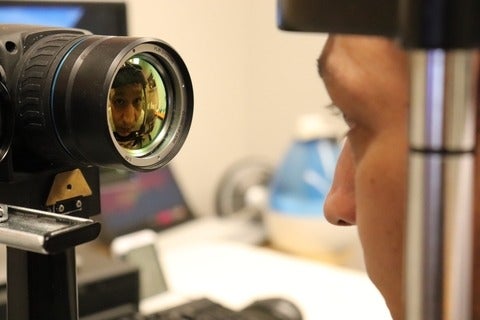A selfie reflection of a researcher looking into a eye testing equipment