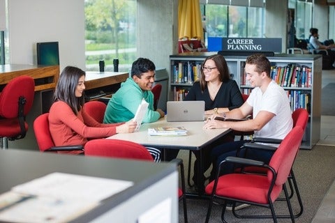 Four students are sitting around a table with a laptop at the centre for career action