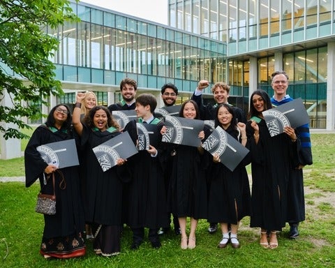 Groyp of SFM gradates in their conovcation robes holding diplomas and celebrating 