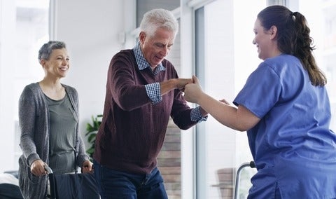 A senior man in a wheelchair standing up with the help of a nurse