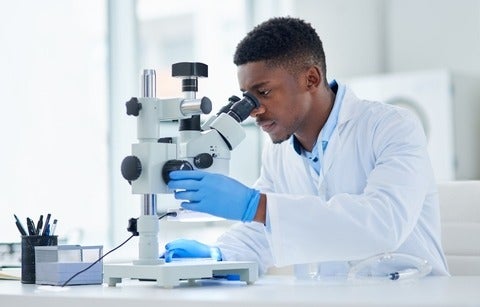 A focused young male scientist looking at test samples through a microscope inside of a laboratory 