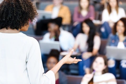 Unrecognizable female professor gestures while teaching diverse college students