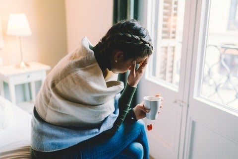 Woman with temperature staying home wrapped in scarf and drinking hot tea
