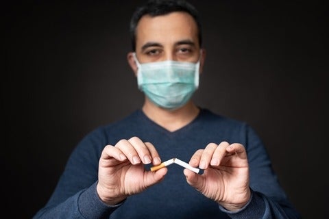 Man with protective face mask breaking cigarette 