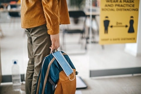 A person holding a knapsack bag and a face mask