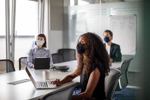 Team of business professionals wearing face mask sitting in office boardroom during a meeting.