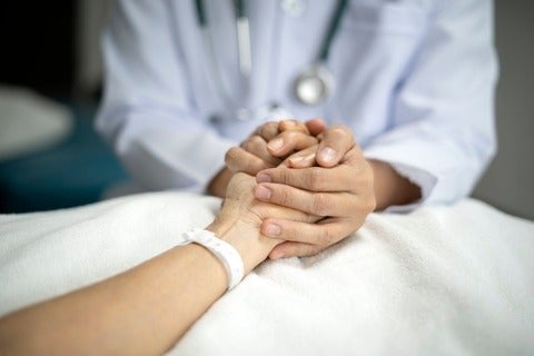 Doctor holding hand of senior female patient to give her support on her hospital bed 