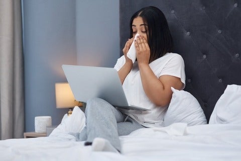 A woman sick in bed at home with a laptop 
