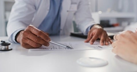 Cropped shot of an unrecognizable doctor sitting and reading test results with his patient during a consultation in his clinic 
