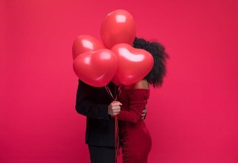 Young couple wearing elegant covering with bunch of heart shaped balloons.