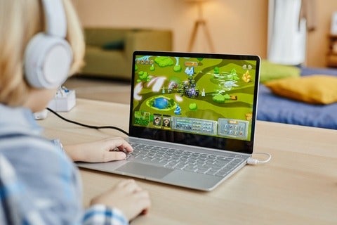 Person with headphones looking on laptop screen with video game displayed. 