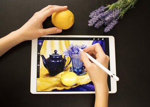 Someone draws a still life picture with teapot, lemon and flowers with a pencil on an electronic tablet.