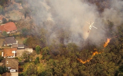 Aerial of water bombing a bushfire from a helicopter