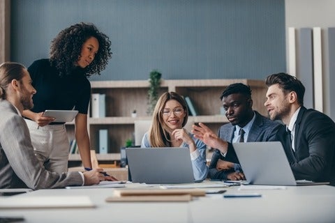Group of people in business attire discussing amongst each other in a room with laptops