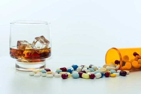 Whiskey glass, with ice cubes, beside a large amount of drugs, capsules and pills