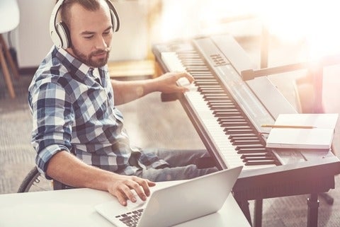 Composer sitting in semi position wearing headphones using laptop while writing new composition