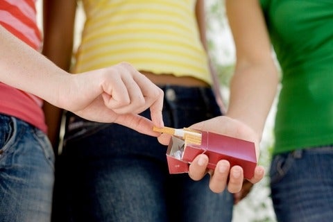 Teenage girl taking cigarette from friend cigarette pack
