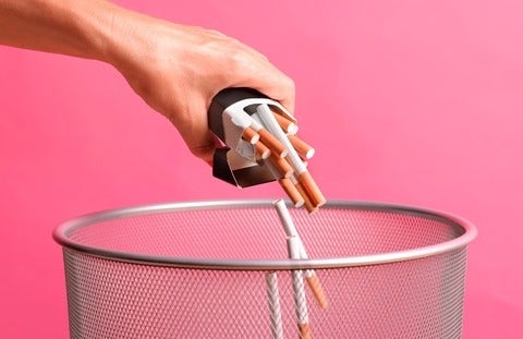 Close up of someone throwing a pack of cigarettes away in a bin