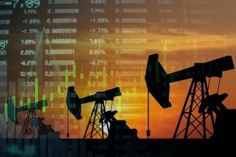 Oil derricks in silhouette with stock prices listed in the background
