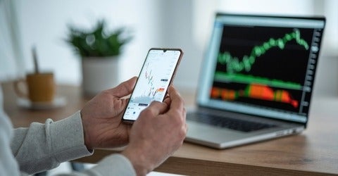A person looking at stock returns on their phone and their laptop