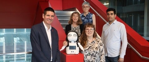 A group of researchers stand together with a social robot