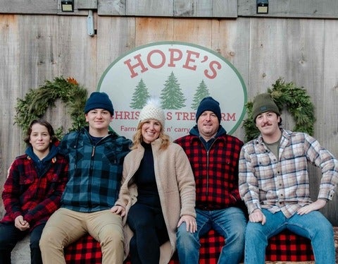 The Hope family sits together on a log with a barn behind them