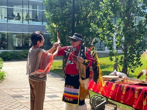Dean Lili Liu and Elder Myeengun Henry hold up an eagle feather